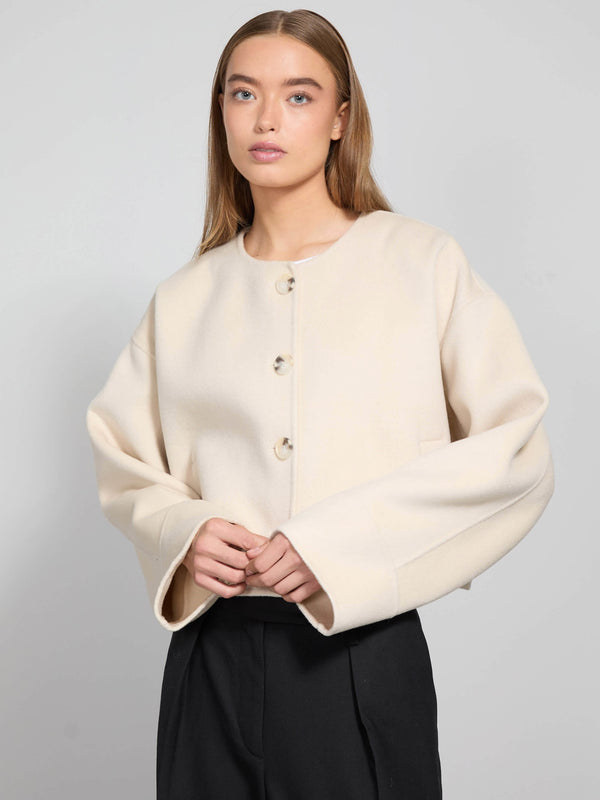 A model wears a cream-colored, oversized jacket with a round neckline and button closure, showcasing a stylish, modern look by MEOTINE.