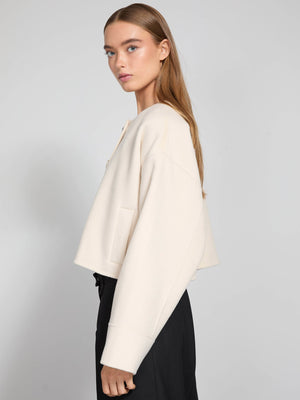 A model showcases a cream-colored cropped jacket with a relaxed fit, paired with black trousers, representing MEOTINE's stylish design.