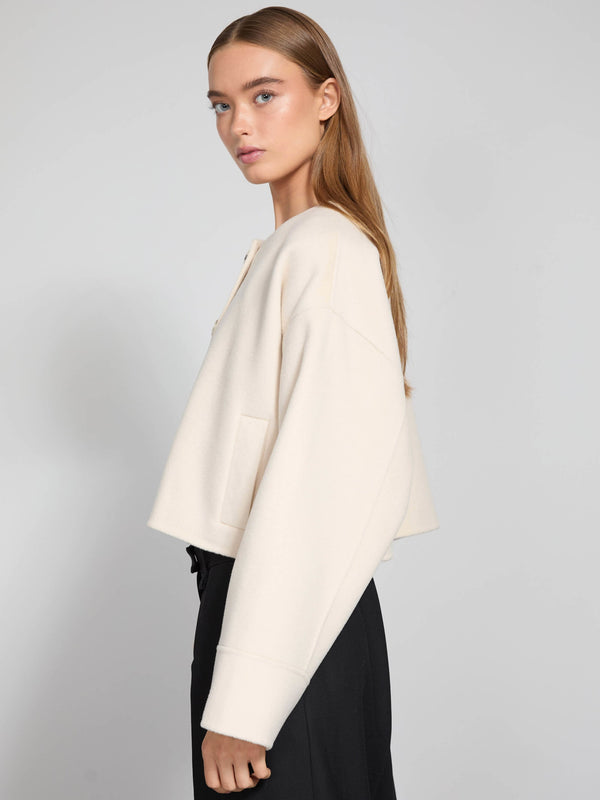 A model showcases a cream-colored cropped jacket with a relaxed fit, paired with black trousers, representing MEOTINE's stylish design.