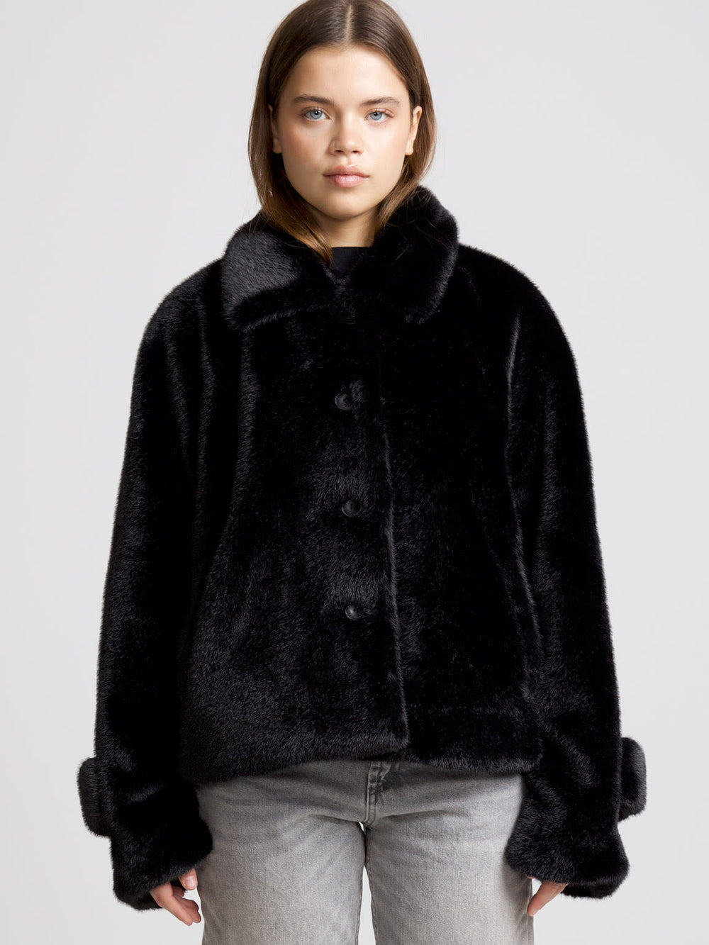 A model showcases a luxurious black faux fur coat by MEOTINE, featuring a wide collar and oversized sleeves, paired with denim.
