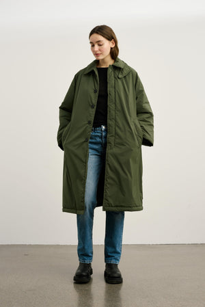 A model wears a long olive green MEOTINE coat over a black top and blue jeans, showcasing a stylish, oversized look.