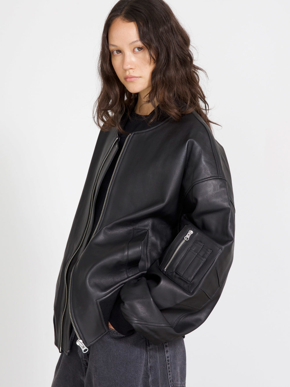 Stylish black leather bomber jacket with a zip front and side pockets, paired with light blue jeans. MEOTINE brand.