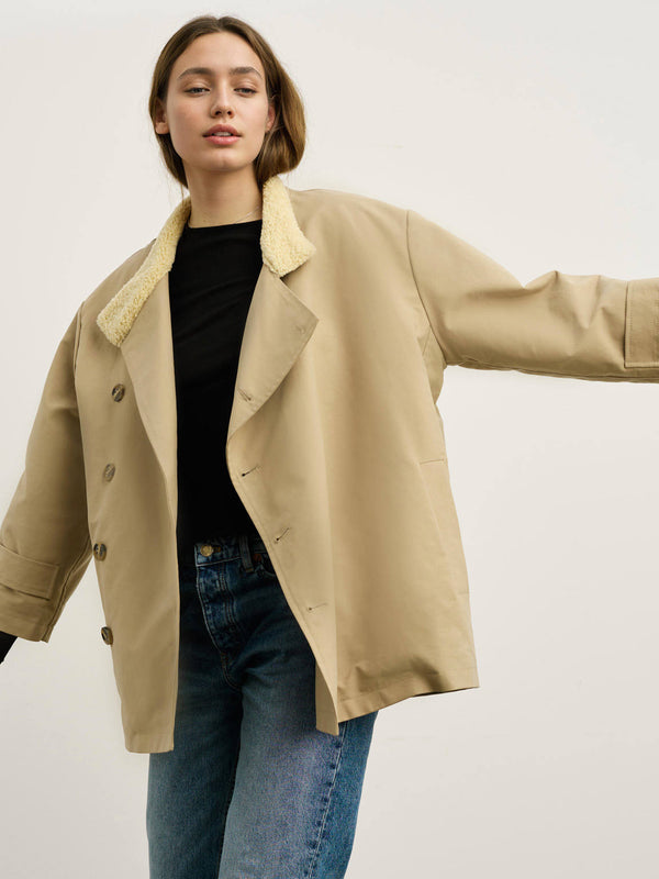 A model showcases a beige oversized jacket with a cozy shearling collar, paired with a black top and blue jeans by MEOTINE.