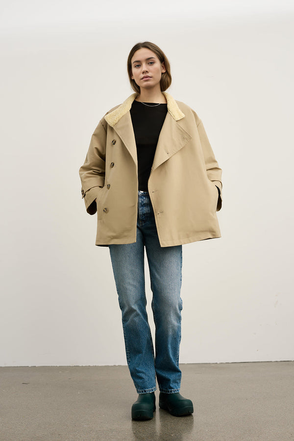 A model wears a beige oversized coat with a soft collar, paired with blue jeans and green clogs, showcasing MEOTINE's stylish design.
