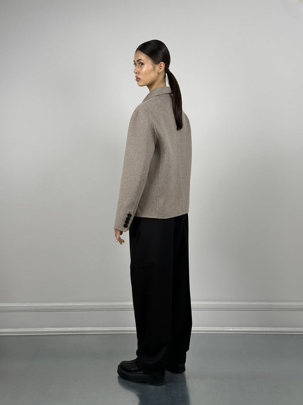 A model showcases a stylish MEOTINE jacket from the back, paired with loose black trousers and sleek black boots.