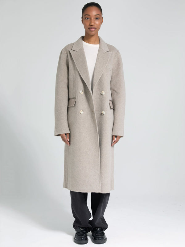 A model showcases a stylish beige double-breasted coat by MEOTINE, paired with a simple white top and black pants.