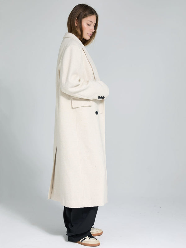 A model showcases a stylish, long cream coat with a tailored fit and side slits, perfect for a chic winter look by MEOTINE.