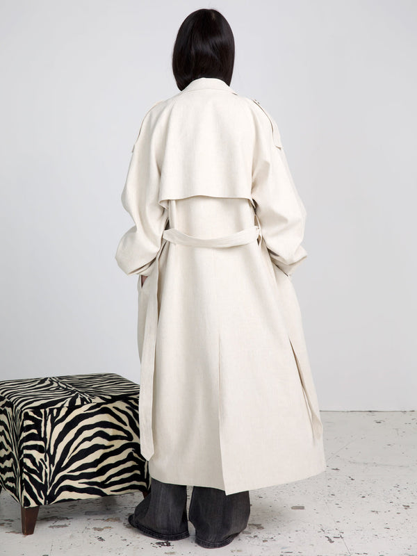 A model wearing a stylish beige trench coat from MEOTINE, showcasing a relaxed fit and elegant design, stands against a neutral backdrop.