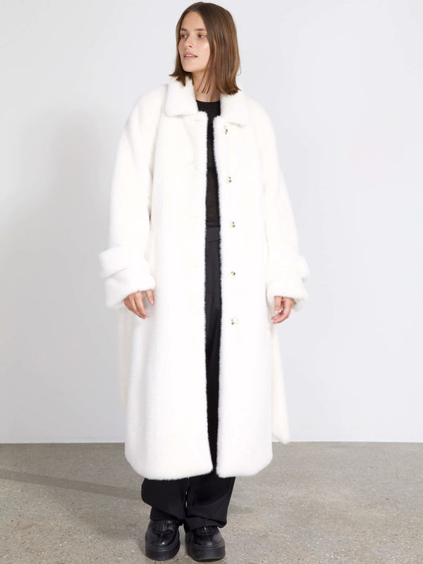 A model wears a cozy white MEOTINE coat with a classic collar and oversized sleeves, styled over a black outfit.