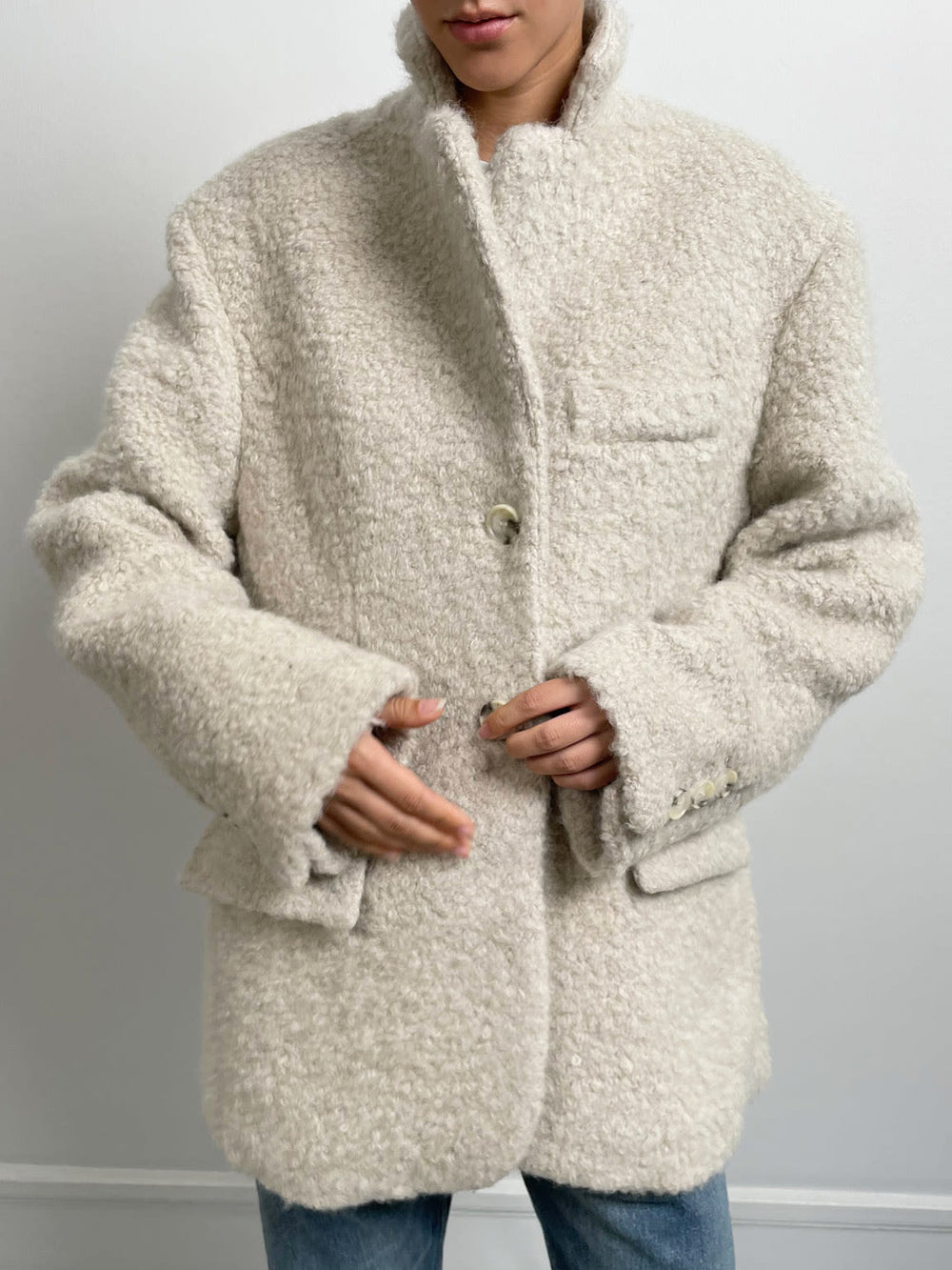 Cozy beige oversized jacket with a textured finish, featuring a notched collar and buttoned front, styled with a simple white tee. MEOTINE.