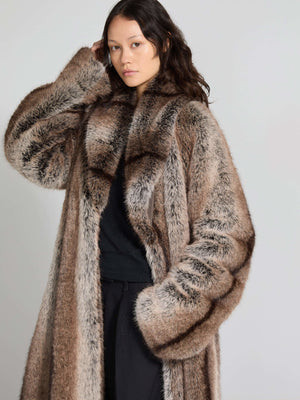 A model showcases a luxurious, oversized faux fur coat in shades of brown and cream, embodying MEOTINE's chic style.