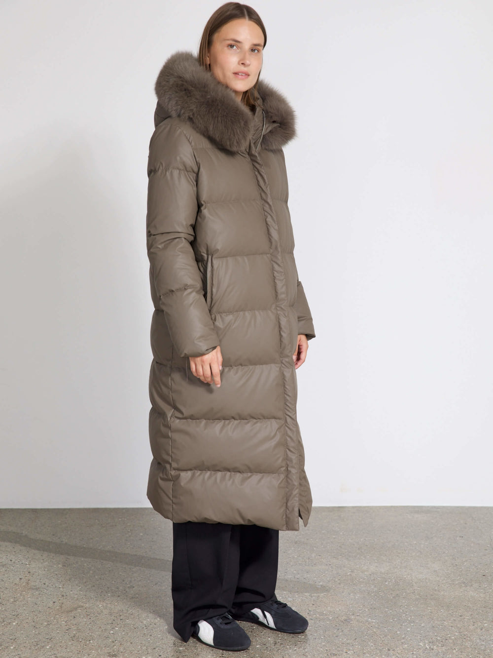 A woman models a long, olive green puffer coat with a fur-lined hood, showcasing MEOTINE's stylish winter outerwear.