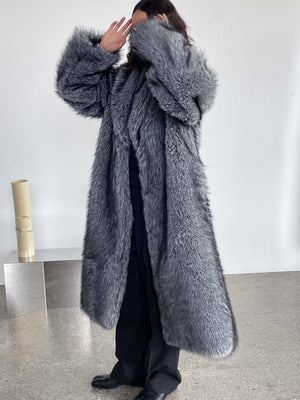 A model wearing a luxurious gray faux fur coat by MEOTINE, styled with black pants, poses against a minimalist backdrop.