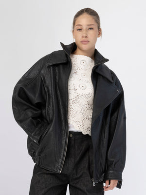 A model wears a stylish oversized black leather jacket from MEOTINE, paired with a white crochet top and dark jeans.