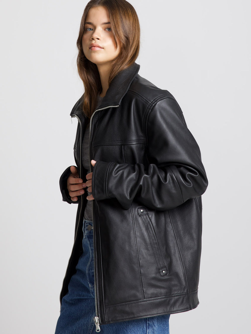A model wearing a black leather jacket from MEOTINE, paired with blue jeans and black boots, posing against a neutral background.