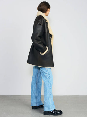 A model showcases a stylish black shearling coat with a cozy cream lining, paired with light blue wide-leg jeans. MEOTINE.