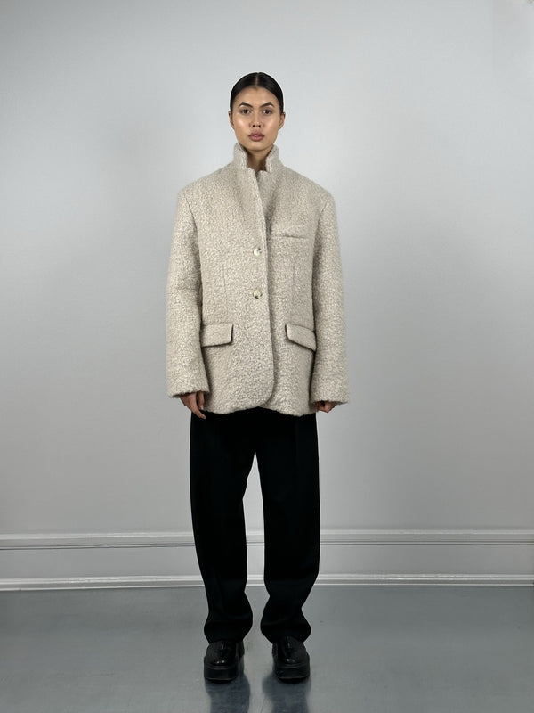 A model showcases a stylish, oversized beige coat with a textured finish, paired with black trousers, representing MEOTINE's chic aesthetic.