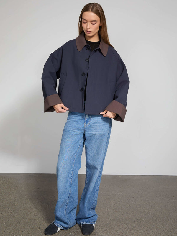 A model wears a stylish navy jacket with brown cuffs, paired with relaxed blue jeans, showcasing MEOTINE's modern design.