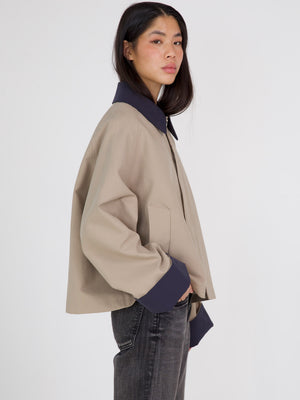A model showcases a stylish beige and navy jacket by MEOTINE, featuring a relaxed fit and modern design, paired with dark jeans.