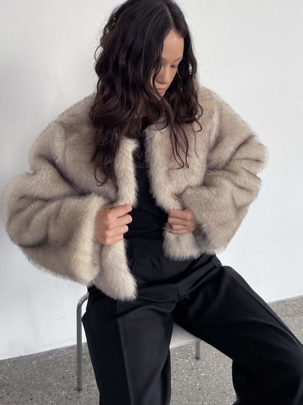 A model wearing a soft, beige faux fur jacket by MEOTINE, styled with black pants, exuding a cozy and chic vibe.
