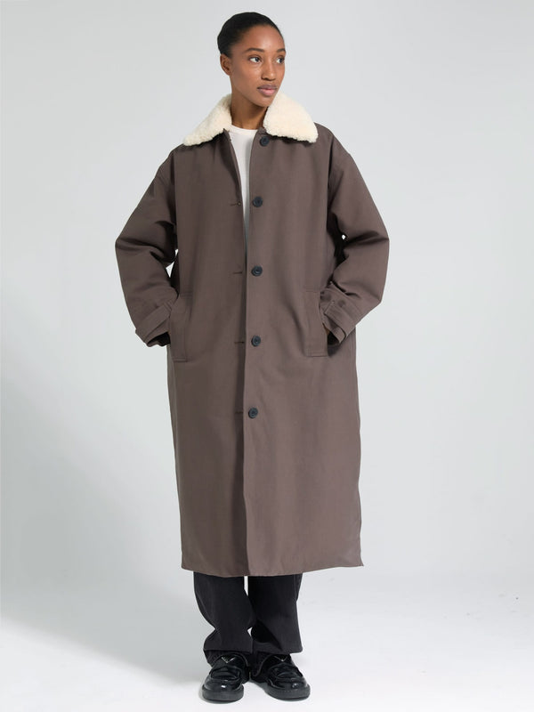 A model stands in a long brown coat with a white fur collar, showcasing MEOTINE's stylish and cozy outerwear design.