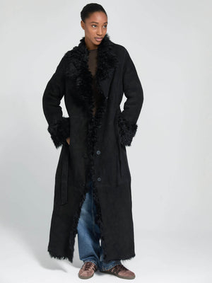 A model wears a long black coat with a fluffy collar and cuffs, styled with loose jeans, showcasing MEOTINE's chic design.