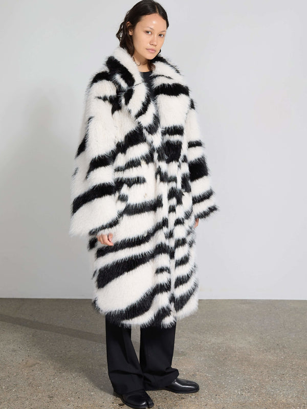 A model showcases a stylish black and white striped faux fur coat by MEOTINE, paired with sleek black trousers.