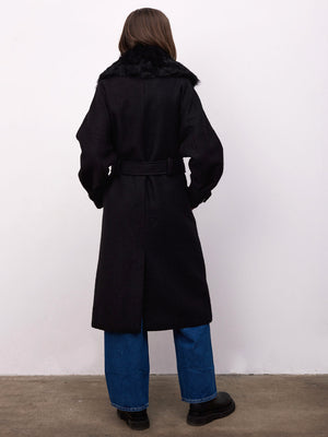 A woman in a black coat with a faux fur collar, belted at the waist, paired with blue wide-leg jeans. MEOTINE style.