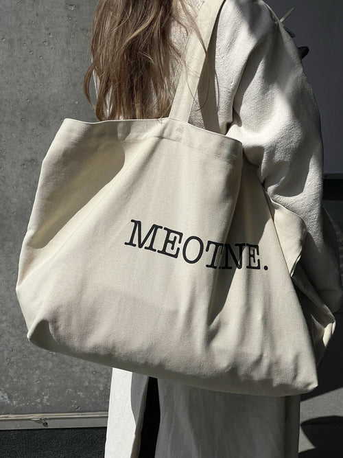 A stylish cream tote bag featuring the brand name "MEOTINE." in bold black letters, perfect for everyday use.