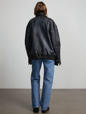 A model wearing a black oversized leather jacket from MEOTINE, paired with light blue jeans, standing against a neutral background.