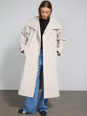 A model wears a stylish beige trench coat with a wide collar, paired with loose blue jeans, showcasing MEOTINE's modern design.