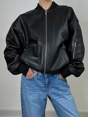 Stylish black leather bomber jacket with a zip front and side pockets, paired with light blue jeans. MEOTINE brand.