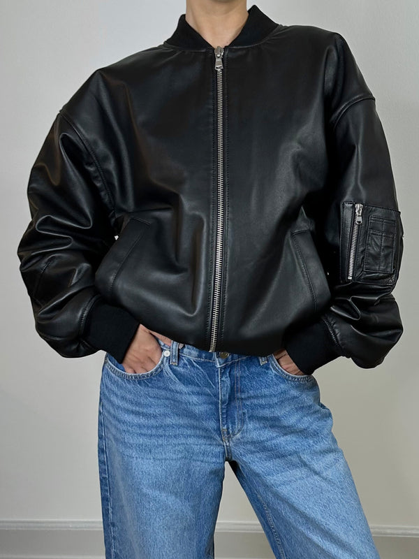 Stylish black leather bomber jacket with a zip front and side pockets, paired with light blue jeans. MEOTINE brand.