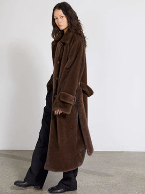 A model showcases a luxurious brown oversized coat by MEOTINE, featuring a classic collar and button closure, styled with black pants.