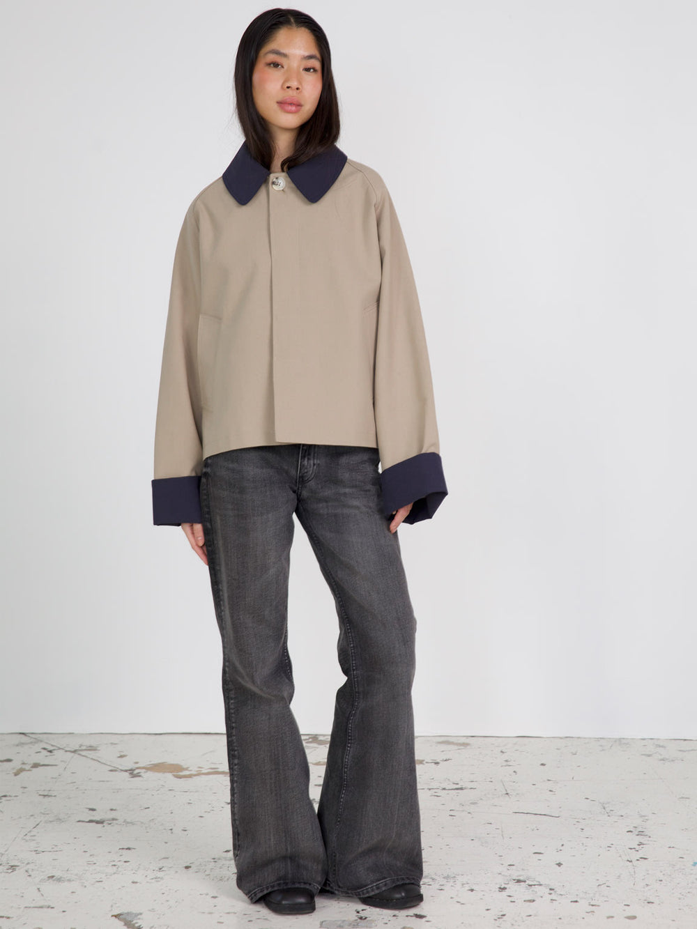 A model showcases a stylish beige jacket with a large collar and navy cuffs, featuring prominent buttons. MEOTINE's chic design stands out.