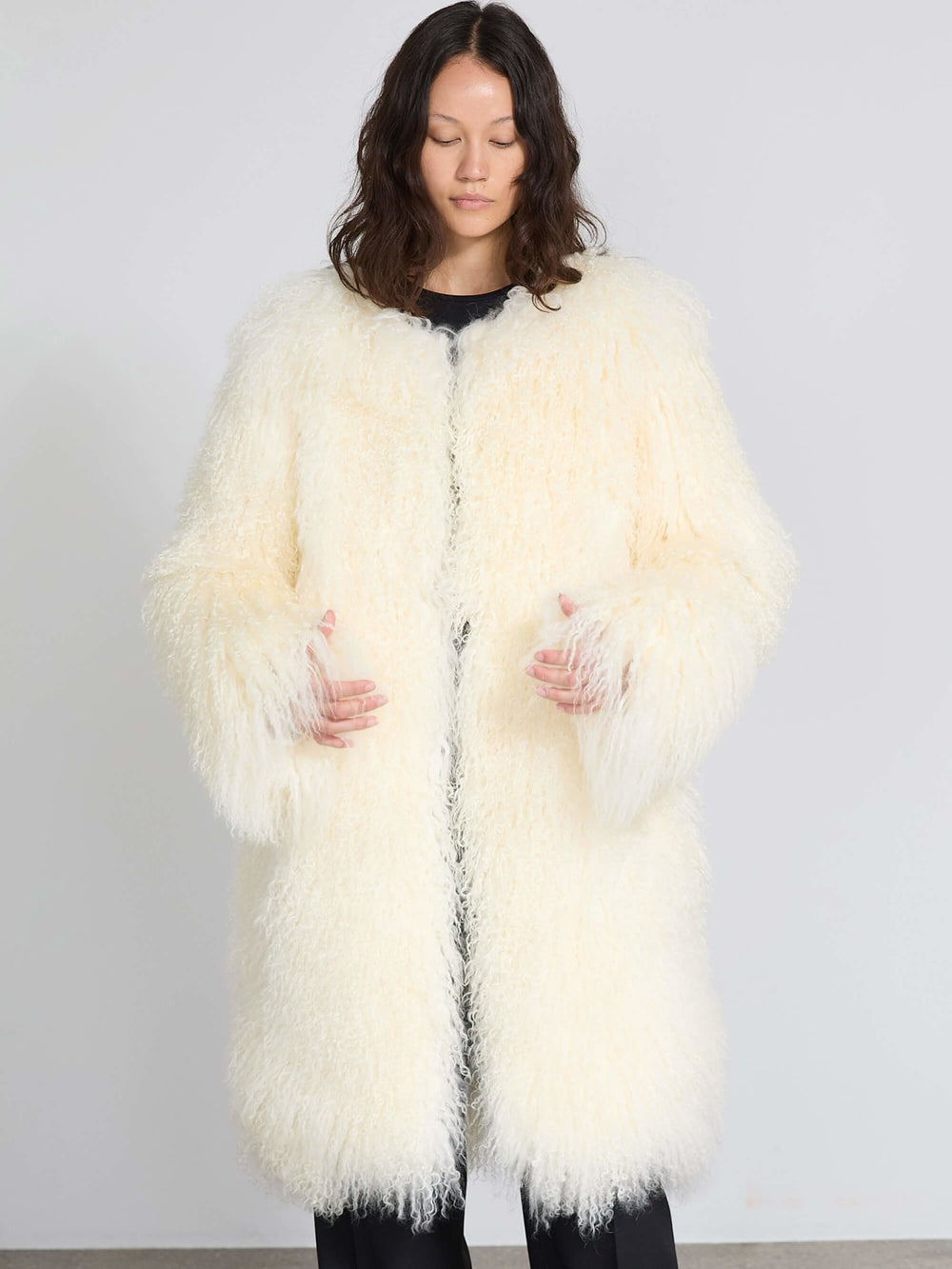 A model sits on a chair wearing a fluffy white MEOTINE sweater paired with black pants, showcasing a cozy and stylish look.