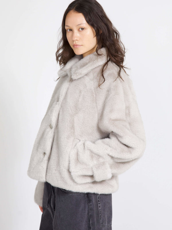 A model showcases a cozy, light gray faux fur jacket with a collar and button closure, perfect for stylish warmth by MEOTINE.