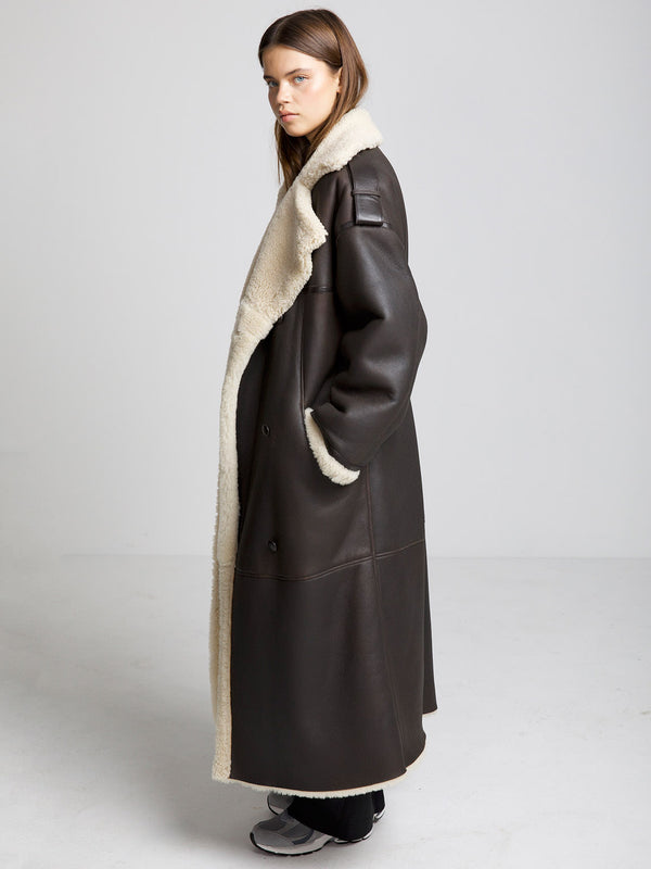 A model showcases a stylish brown MEOTINE coat with a plush cream shearling lining, exuding warmth and elegance.