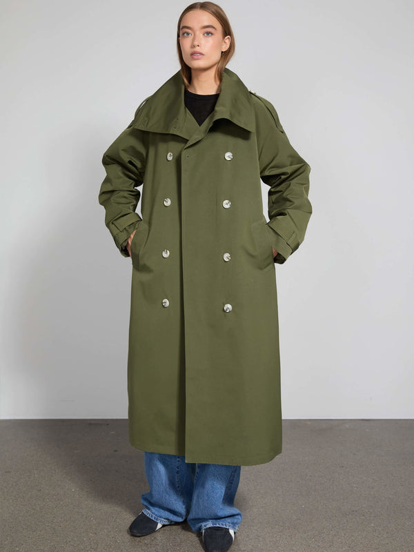 A model showcases a stylish olive green trench coat with a double-breasted design, featuring large buttons and side pockets by MEOTINE.