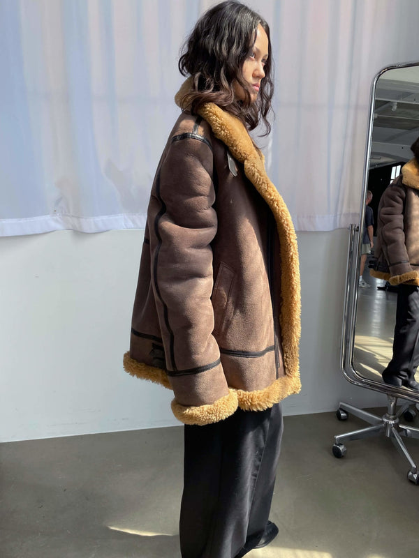 A model showcases a brown shearling jacket with a cozy fur collar, styled with black pants, reflecting MEOTINE's chic aesthetic.