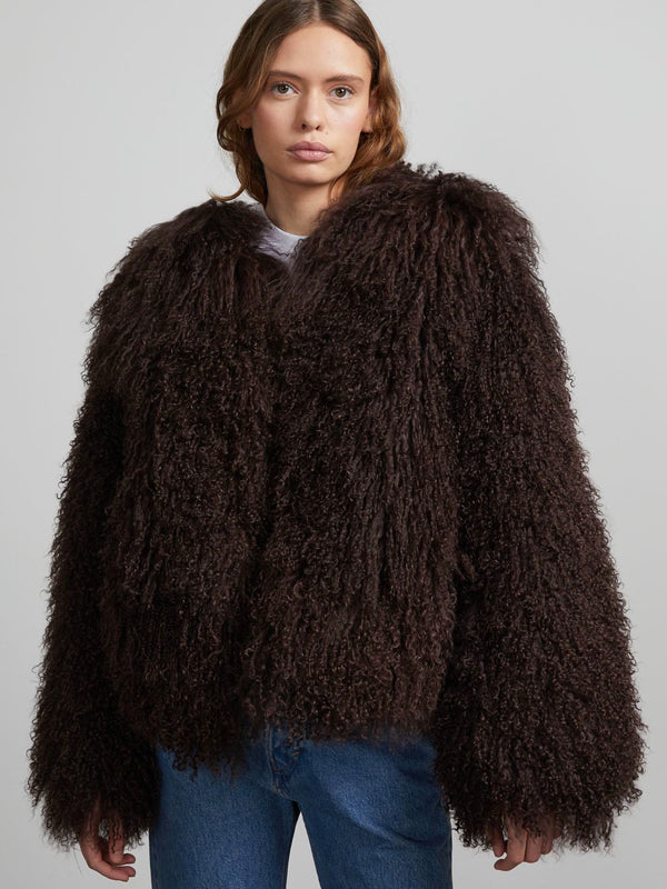 A model wears a cozy, oversized brown curly fur jacket by MEOTINE, paired with casual blue jeans against a neutral background.