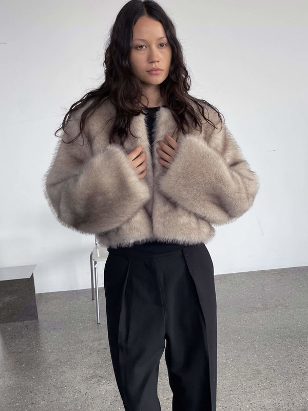 A model showcases a stylish, cropped fur coat in soft beige, paired with black high-waisted trousers, embodying MEOTINE's chic aesthetic.