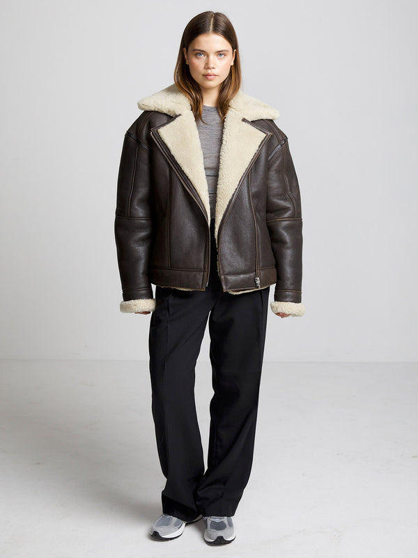A model wearing a brown shearling jacket with a cozy collar, paired with black pants and sneakers, showcasing MEOTINE's stylish outerwear.