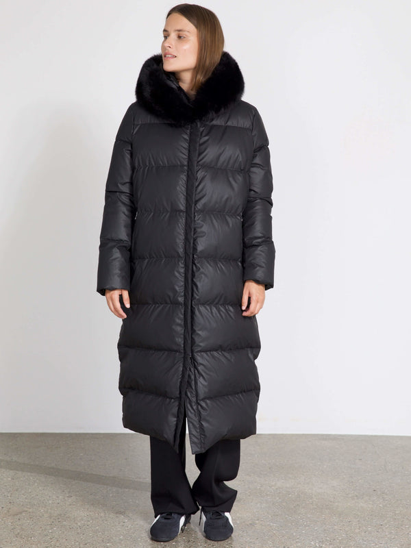 Long black puffer coat with a luxurious fur collar, worn by a model standing against a plain background. MEOTINE brand style.