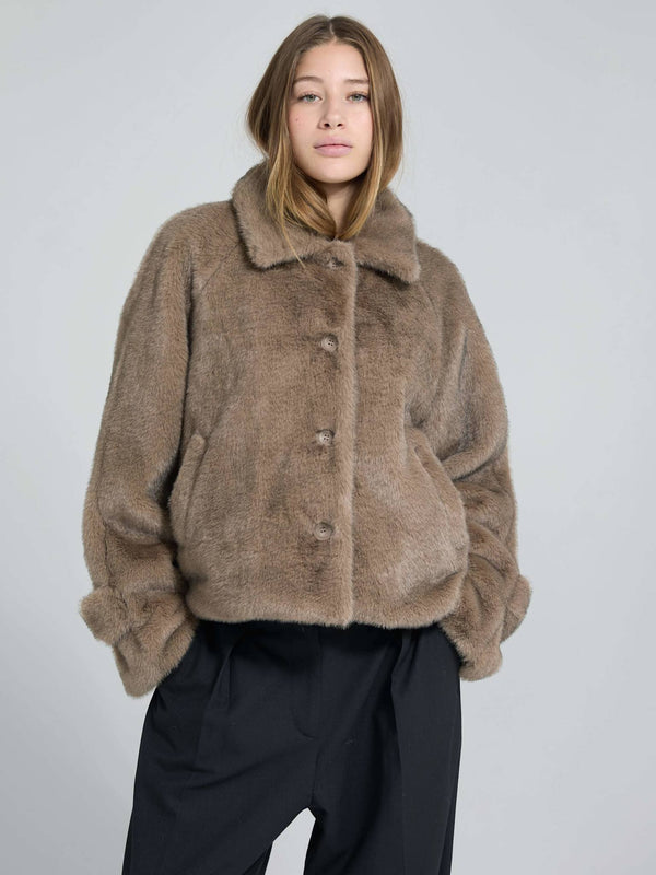 Cozy brown faux fur jacket with a collar and button closure, styled with loose black trousers, perfect for a chic winter look. MEOTINE.