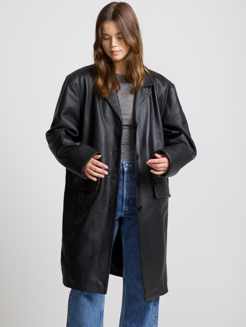 A model wears a stylish black leather coat from MEOTINE, paired with a gray top and blue jeans, showcasing a chic look.