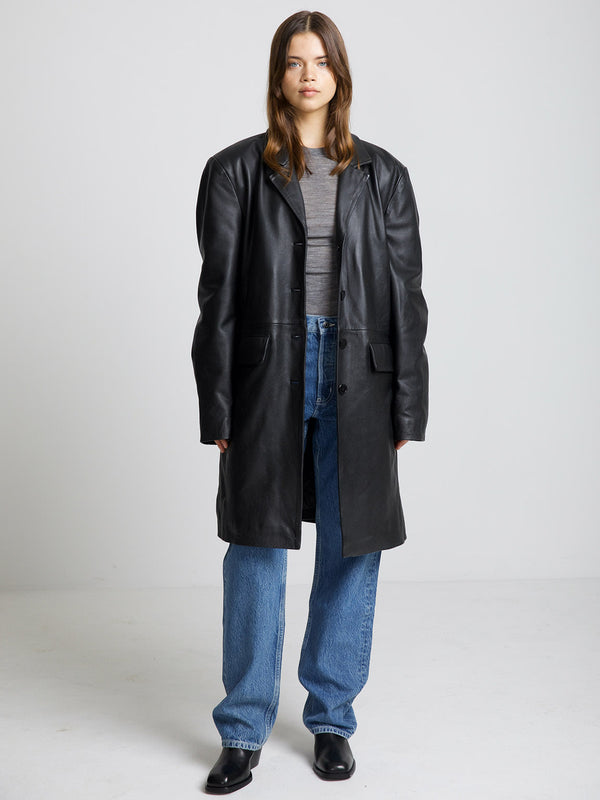 A model wears a stylish black leather coat over a gray top, paired with blue jeans and black shoes, showcasing MEOTINE's chic design.