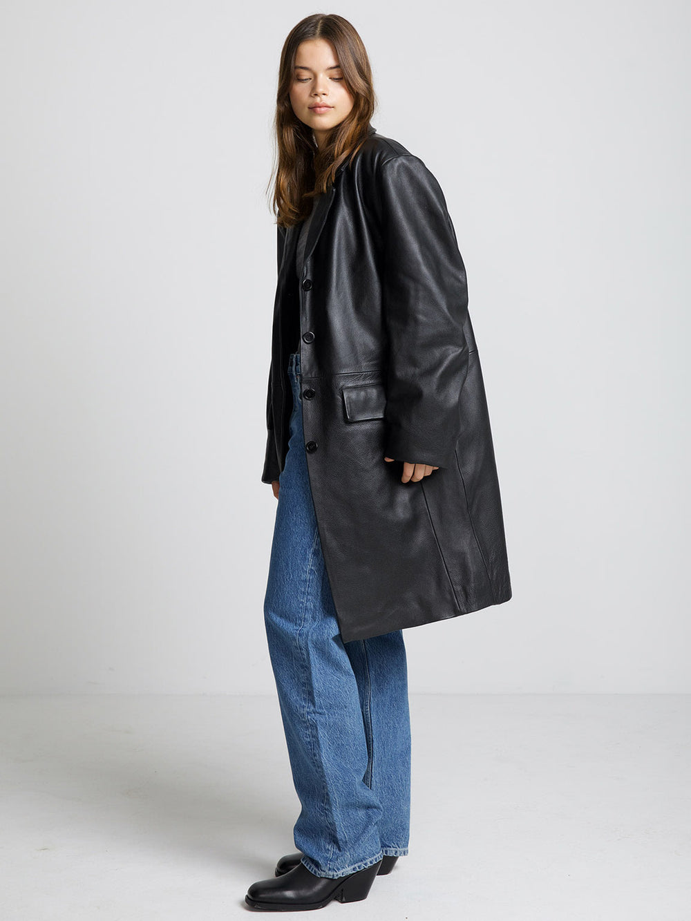 A model wears a stylish black leather coat from MEOTINE, paired with a gray top and blue jeans, showcasing a chic look.