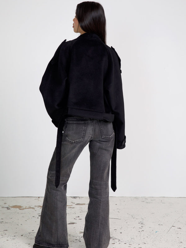 A model showcases a stylish black cropped jacket with a unique design, paired with flared gray jeans, representing MEOTINE's chic aesthetic.