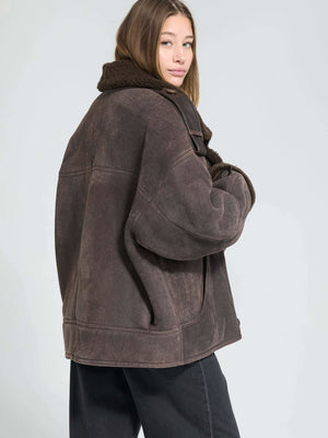 A model showcases a cozy brown MEOTINE jacket with a plush collar, styled with relaxed black pants against a neutral backdrop.